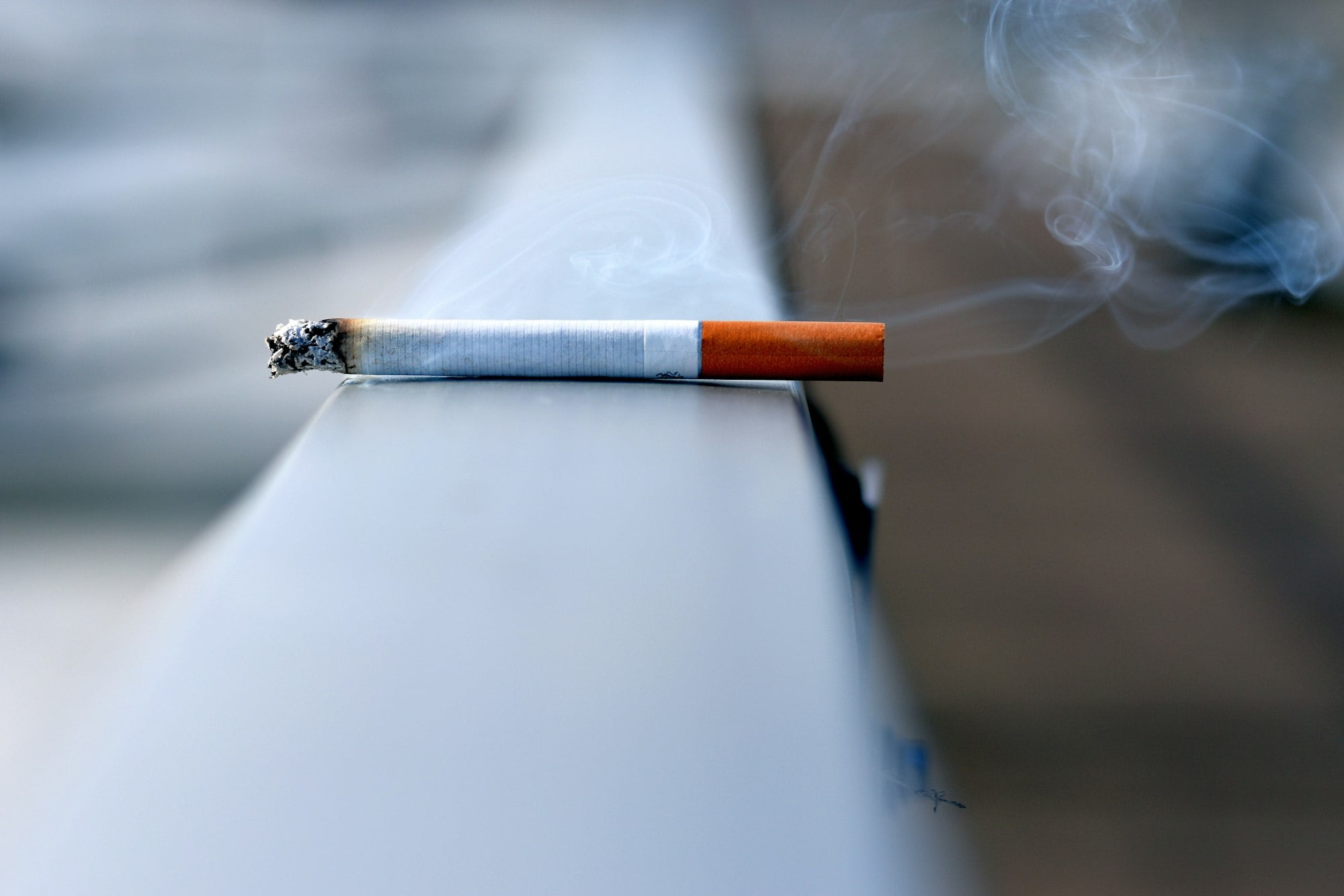 A lit cigarette resting on a ledge, representing tobacco prevention work